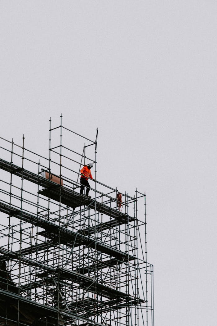 A construction worker in safety gear on scaffolding at a building site.